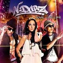 A portrait of three young adults walking in an urban environment at night. On the left and right are young men wearing sunglasses, and in between them is a brunette woman in a white dress. Above them is a N-Dubz logo in white and below it is the title 'Love.Live.Life' in white capital letters.