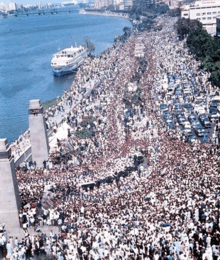 Throngs of people marching in a thoroughfare that is adjacent to a body of water