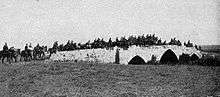 Photo of mounted rifles brigade crossing a three arched stone bridge.