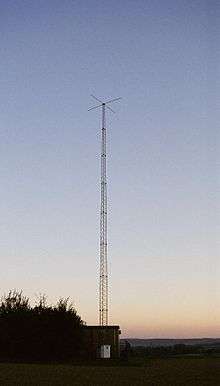 Tall antenna tower on a background of twilight clear sky; small shack is at bottom of tower