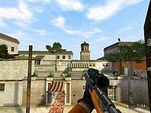 Screenshot from a first-person perspective, showing the player's character on a mission, looking out from a window, at a hotel across the street in Morocco. An assassin can be seen on a rooftop, getting ready to assassinate a person.