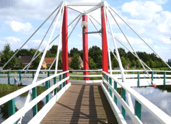 Red-white-green bridge over water reflecting clouds with houses and trees in the background
