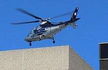 Blue sky, silver helicopter about to land on a stone or concrete building