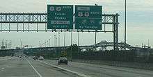 A multilane freeway approaching a bridge. In the foreground, there are two overhead green signs with the one on the left reading U.S. Route 1/U.S. Route 9 north Pulaski Skyway No Trucks next left and the one on the right reading Truck U.S. Route 1/U.S. Route 9 north New Jersey Turnpike Interstate 95 N.J. Turnpike