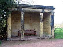 A open stone structure with four columns supporting a lintel. Inside the loggia is a wooden seat.