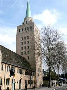 A tall light-coloured stone square tower with a small metal spire; to the left, a smaller building in the same stone with a dark tiled roof