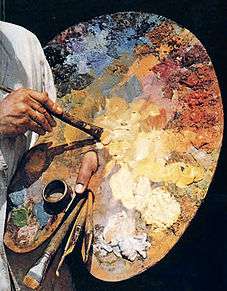 A man's finger sticks through a hole in a large wooden palette. One of his hands is dipping a brush into the paint and the other holds numerous brushes in reserve.