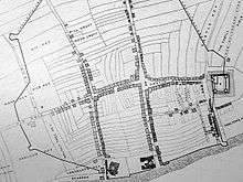 A black and white map, showing a town with a central street, criss-crossed by two adjoining small roads and a small castle on the far right of the map.