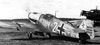 A black and white photograph a propeller driven fighter aircraft viewed from the rear-left. The aircraft is on a grass field, engine appears to be running. It bears three black and white crosses, two on the upper wings and one on the left side of the fuselage besides a large number "2". The tail rudder shows a black swastika plus rudder bears approximately 33 small vertical black lines arranged in three groups of varying length.