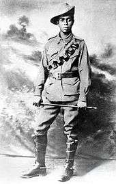 An Aboriginal soldier wearing a slouch hat, leather chest pouches and riding boots, holding a cane