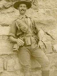An informal, sepia portrait of a man in military uniform. He is leaning against what appears to be a wall.