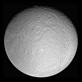 A spherical body is almost fully illuminated. The terminator is running near the top edge. The surface is covered by numerous craters. Two partially overlapping large craters can be seen above the center. One that is younger is above and to the right from the older one.