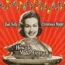 A sepia coloured image of a woman presenting a platter containing a large roast bird (possibly a turkey). Her smiling face is visible beyond the bird, her fingers appear below the platter. The background is red. A strand of coloured Christmas lights stretches across the top of the image. The artist’s name is located to the left of the woman’s head and the words, Christmas Single, are to her right. The title of the single is written over the image of the roast bird.