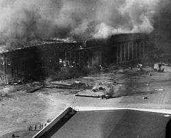 A burning hangar with destroyed planes scattered in front