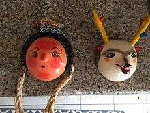A red woman's face with a fish on her head and a wolf painted onto coconut husks