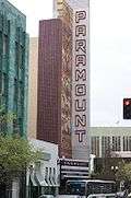 Photograph of a tall sign and mosaic announcing the Paramount Theatre standing above the marquee and a busy street.