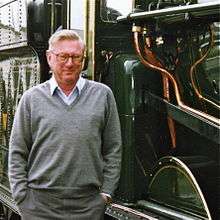 Colour photograph of man in grey pullover standing close to dark green steam locomotive (Great Western Railway King Edward I), with copper pipes showing on side of locomotive.