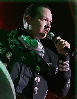 An man singing to a microphone and wearing a charro suit.