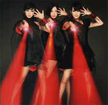 Three members of Perfume in black dresses, pointing three laser beams towards the camera.
