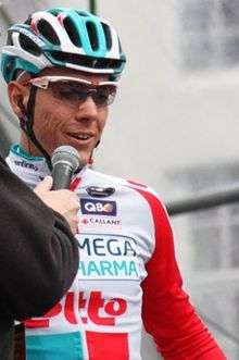 A man of about thirty wearing a cycling jersey and matching helmet that are red, white, and two tones of blue.