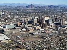 photo taken from an aircraft showing the tall buildings of downtown Phoenix, with the mountains which surround the city in the background.