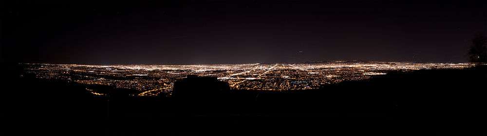 The Phoenix skyline at night from South Mountain. Almost everything in the foreground is darkened, but there are lights in the center and the background, which delineate streets and buildings.