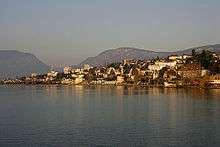 A collection of houses and other small buildings scatter the shore of a wide lake