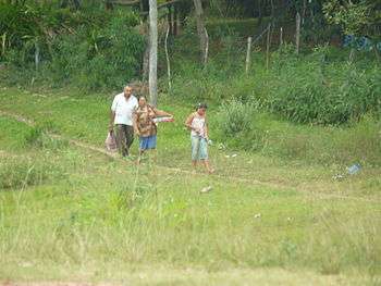 Man, woman and young girl carrying packages on dirt path