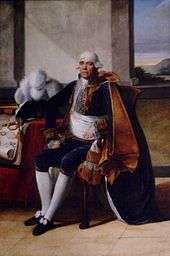 Painting of a seated man in Imperial Court dress with an old-style powdered wig. He wears a red cape over a dark blue coat and breeches with white knee stockings.