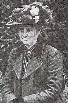 Black and white photograph dated 1912 of a middle-aged Beatrix Potter wearing a flowered hat turned slightly to her right and looking away from the photographer