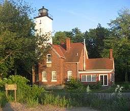 A brick house with a white, square lighthouse tower attached to the house.