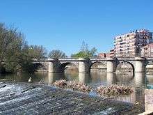 Photo depicts a stone bridge with five arches crossing a river.