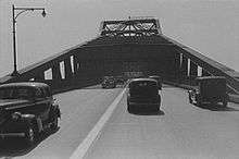 A grayscale photo of a four lane undivided road on a bridge