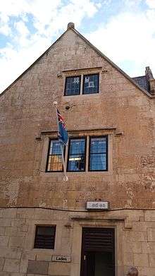 A medieval stone building, with an RAF flag flying from the front. Approximately twenty feet up, in the centre of the building's front face, an iron cannonball about 4 inches in diameter is embedded halfway into a cratered part of the stonework.