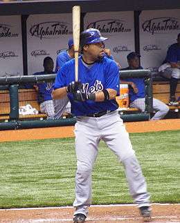 A man in a blue baseball jersey and white pants enters a right-handed batting stance.