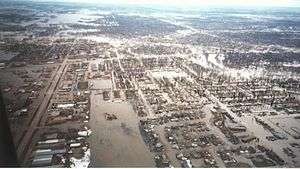 An overhead view of neighborhoods surrounded by water. The flooding can be seen for several miles.