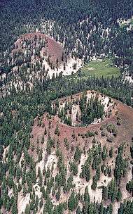 Two red cinder cones in a forest. There is a meadow at the base of one of the ones