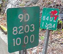 Two nearly adjacent markers, one slightly defaced with red ink, with slightly different sets of numbers