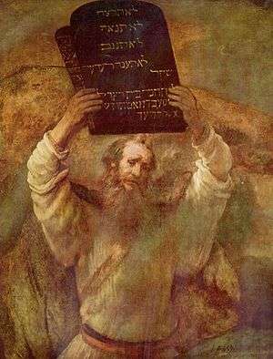 This is an image of an oil on canvas picture by Rembrandt (1659) of a bearded man representing Moses with two tablets of stone of the ten commandments held high in both hands.