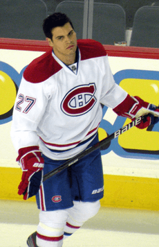 A hockey player with short dark hair looks to his right as he skates.  He is in a white uniform with red and blue trim, the number 27 on his arms and a stylized "CH" logo on his chest.