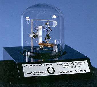 Bell jar covering assembly of plastic and wires, on an engraved plaque commemorating 50 years of the transistor