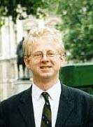 A blond man outside in glasses and a suit and tie
