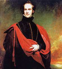 A three-quarter length portrait of a standing man wearing a black cloak with gold buttons, and a red stole with tassels
