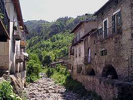 Photo of a dry, rocky streambed running straight through a town of old buildings