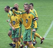 Five men standing on a grass football pitch, wearing yellow shirts, green shorts and yellow socks.