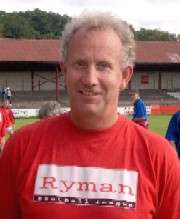 A middle-aged man with curly grey hair, wearing a red T-shirt with "Ryman Football League" printed on it