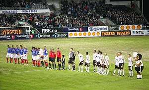 A line of footballers, in blue and white, respectively, at a large stadium