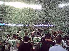 Green and white confetti floats through the air as several players and team staff celebrate a victory.