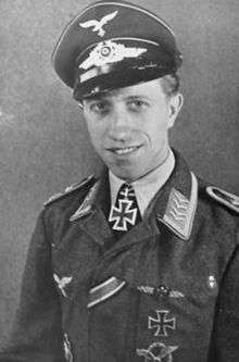 The head and upper body of a young man, shown in semi-profile. He wears a peaked cap and military uniform with various military decorations, at his neck, an Iron Cross displayed at the front of his white shirt collar.