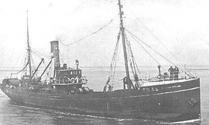 A black-and-white photo showing a little trawler stationary in the water.